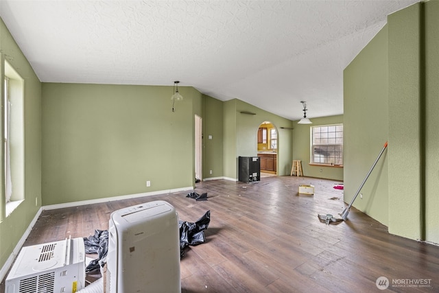 living area with lofted ceiling, a textured ceiling, arched walkways, wood finished floors, and baseboards