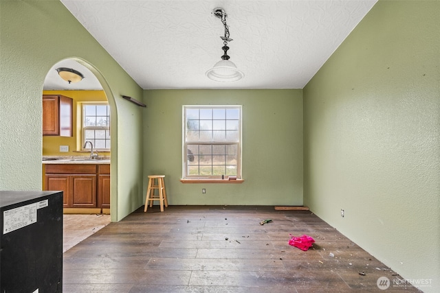 unfurnished dining area with arched walkways, a textured wall, a textured ceiling, a sink, and hardwood / wood-style floors