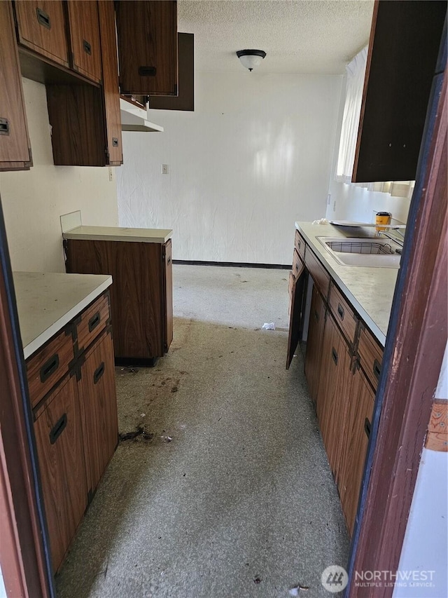 kitchen with a textured wall, light countertops, a sink, and a textured ceiling