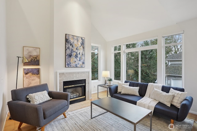 living room with light wood finished floors, baseboards, high vaulted ceiling, and a tiled fireplace