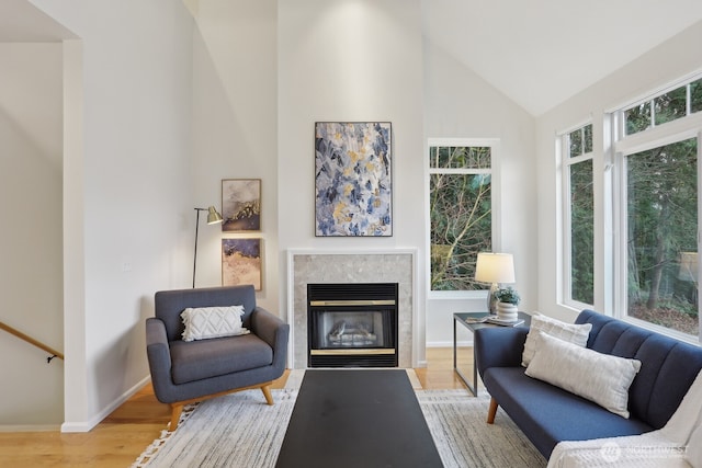 sitting room with high vaulted ceiling, a glass covered fireplace, light wood-style flooring, and baseboards