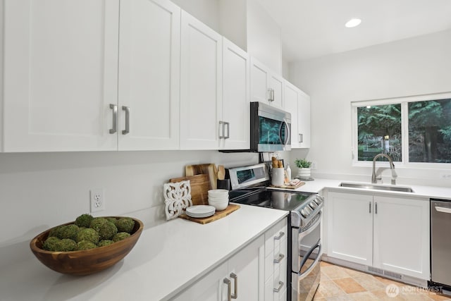 kitchen featuring stainless steel appliances, light countertops, white cabinetry, a sink, and recessed lighting