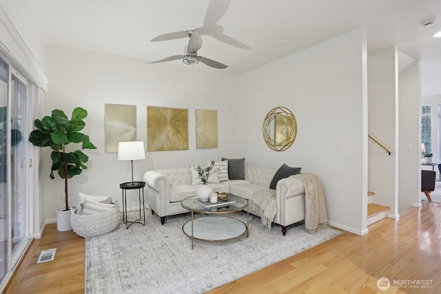 living room with a ceiling fan, stairs, baseboards, and wood finished floors