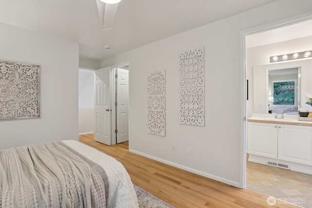 bedroom featuring light wood-type flooring, baseboards, a sink, and ensuite bath