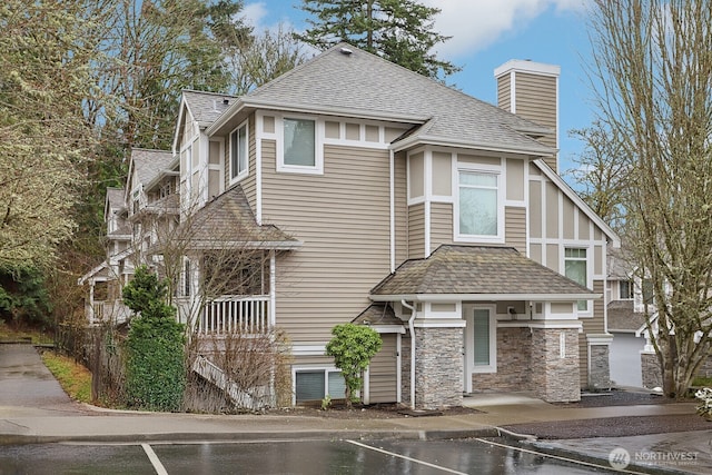 view of front of property featuring a shingled roof, stone siding, and a chimney