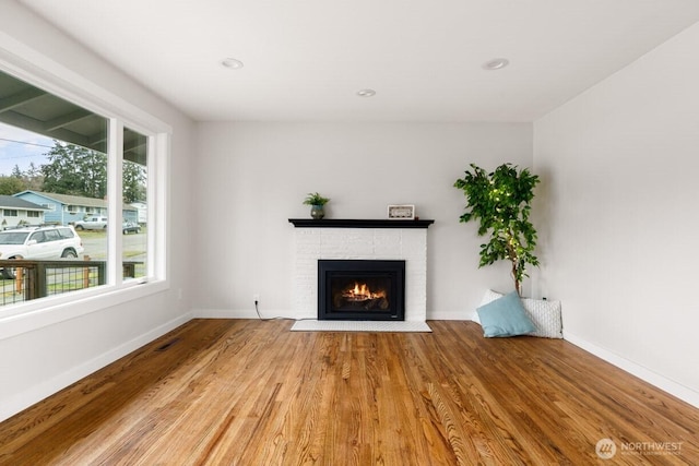 unfurnished living room featuring a brick fireplace, baseboards, wood finished floors, and recessed lighting