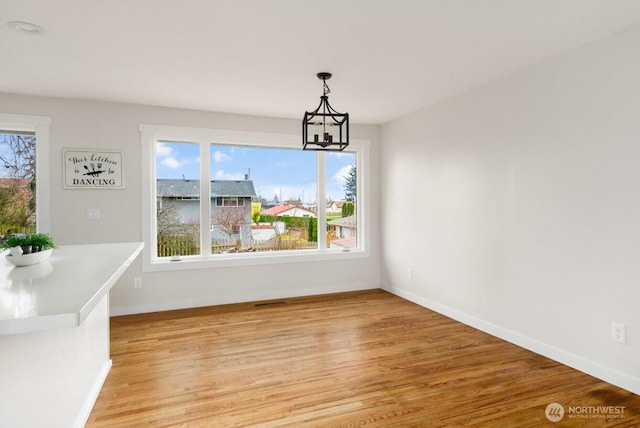 unfurnished dining area featuring light wood-style floors, a healthy amount of sunlight, baseboards, and an inviting chandelier