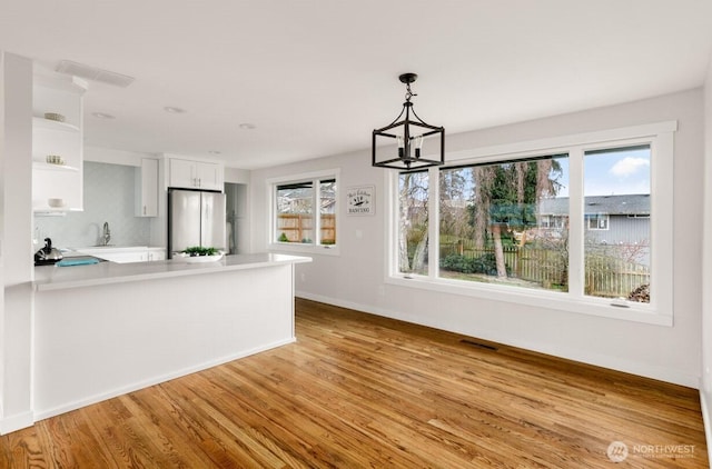 unfurnished dining area with baseboards, visible vents, wood finished floors, a chandelier, and a sink