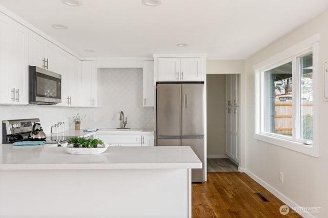 kitchen with visible vents, a peninsula, stainless steel appliances, light countertops, and a sink