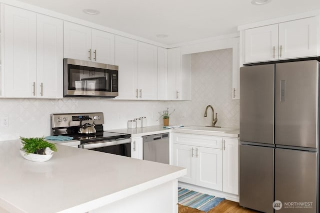 kitchen with white cabinets, appliances with stainless steel finishes, a peninsula, light countertops, and a sink