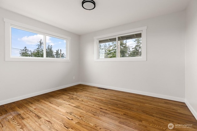 spare room with light wood-type flooring, visible vents, and baseboards