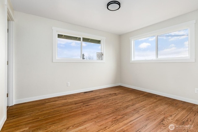 empty room featuring light wood finished floors, visible vents, and baseboards