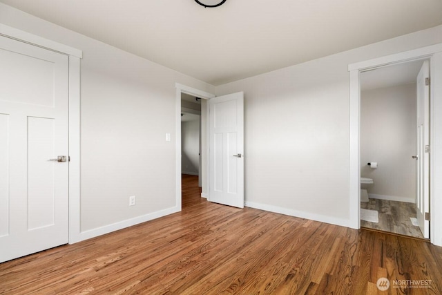 unfurnished bedroom featuring ensuite bathroom, baseboards, and wood finished floors