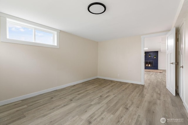 empty room featuring light wood-type flooring, a brick fireplace, and baseboards