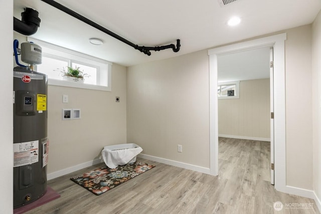 interior space with laundry area, water heater, baseboards, and light wood finished floors