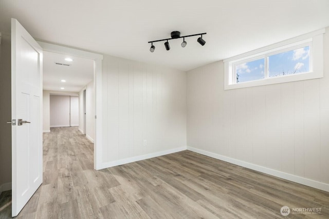 spare room featuring track lighting, light wood-style flooring, and baseboards