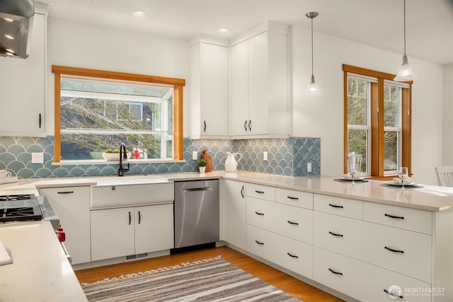 kitchen featuring light wood finished floors, dishwasher, a peninsula, hanging light fixtures, and a sink