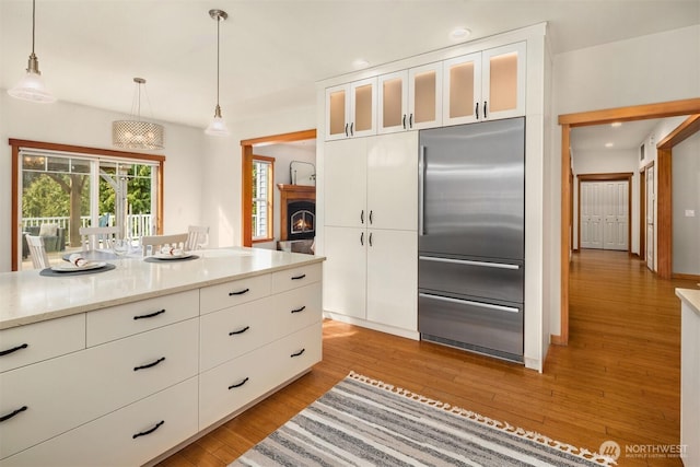 kitchen featuring hanging light fixtures, light wood finished floors, built in refrigerator, and white cabinets