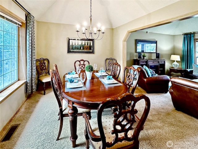 carpeted dining space with a notable chandelier, visible vents, vaulted ceiling, and arched walkways