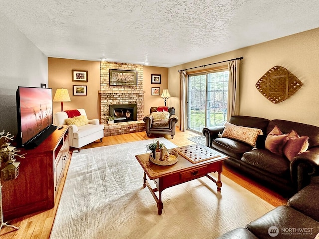 living room featuring a textured ceiling, light wood-type flooring, and a brick fireplace