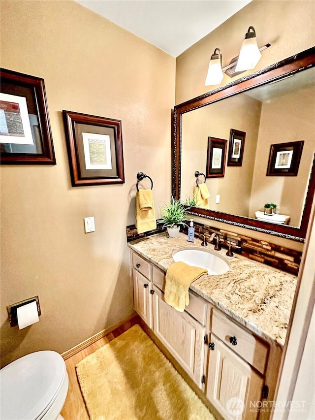 bathroom with wood finished floors, vanity, toilet, and baseboards