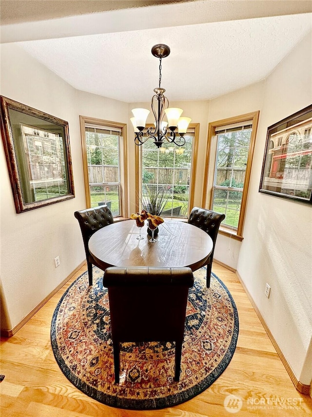 dining room featuring a chandelier, a textured ceiling, baseboards, and light wood-style floors