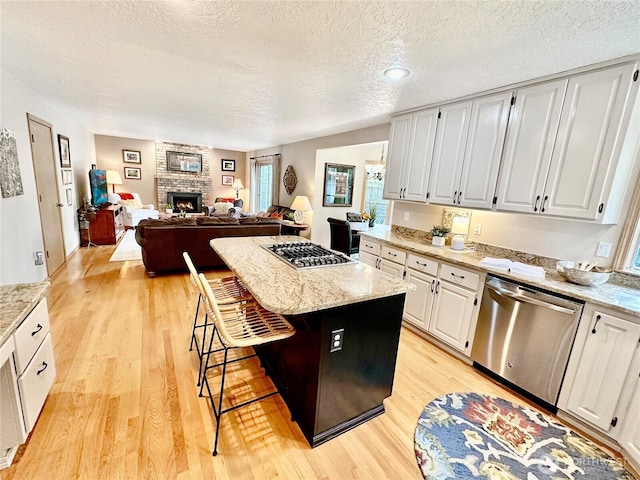 kitchen featuring light stone counters, a fireplace, light wood-style flooring, appliances with stainless steel finishes, and a kitchen island