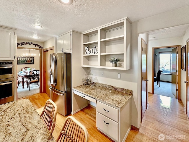 kitchen featuring light wood-type flooring, white cabinets, stainless steel appliances, and built in study area