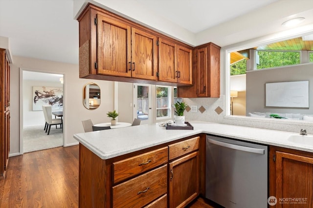 kitchen with a peninsula, light countertops, stainless steel dishwasher, dark wood-style floors, and brown cabinetry