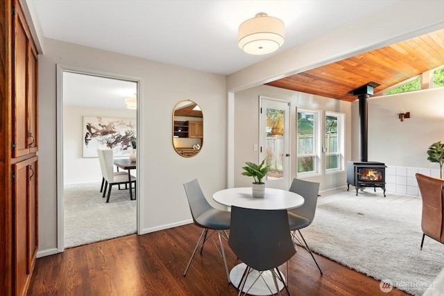 dining space featuring a wood stove, baseboards, dark wood-style flooring, and lofted ceiling