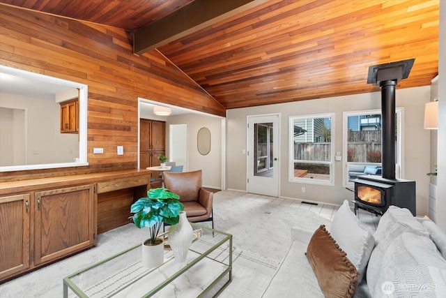 living area with a wood stove, light colored carpet, vaulted ceiling with beams, and wooden ceiling