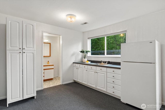 kitchen with freestanding refrigerator, white cabinets, a sink, and visible vents