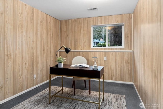 carpeted home office with visible vents, wooden walls, and baseboards