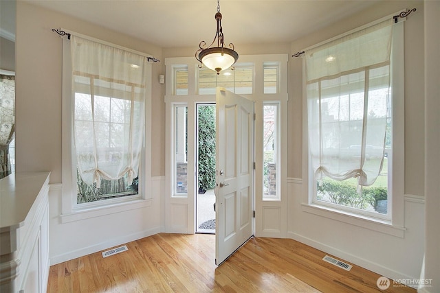 foyer entrance featuring light wood finished floors, visible vents, and wainscoting