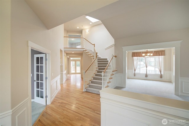 entrance foyer featuring stairway, french doors, light wood-style floors, wainscoting, and a chandelier