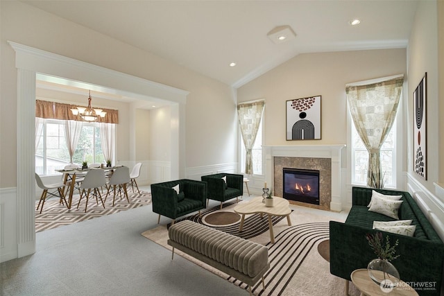 living area featuring carpet floors, a fireplace, wainscoting, a chandelier, and vaulted ceiling