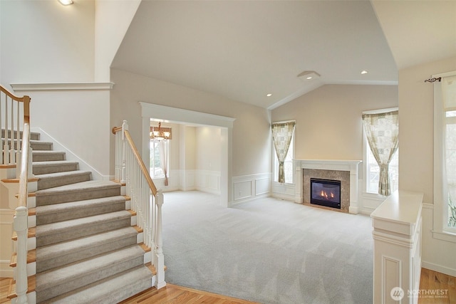 unfurnished living room featuring a wealth of natural light, a decorative wall, lofted ceiling, and a wainscoted wall