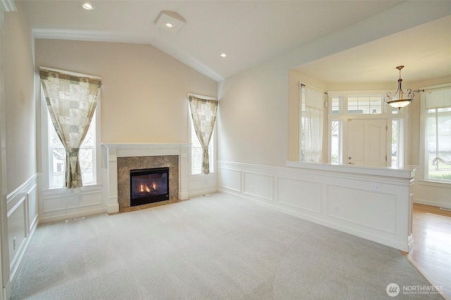 unfurnished living room featuring visible vents, light colored carpet, lofted ceiling, a fireplace, and a decorative wall