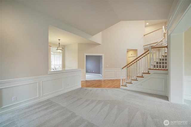 carpeted empty room featuring lofted ceiling, stairway, and a decorative wall