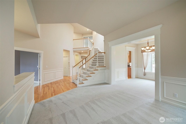 interior space with a decorative wall, a notable chandelier, a wainscoted wall, and carpet floors