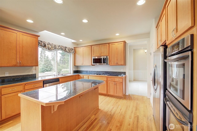 kitchen with a kitchen island, a kitchen bar, recessed lighting, light wood-style flooring, and appliances with stainless steel finishes