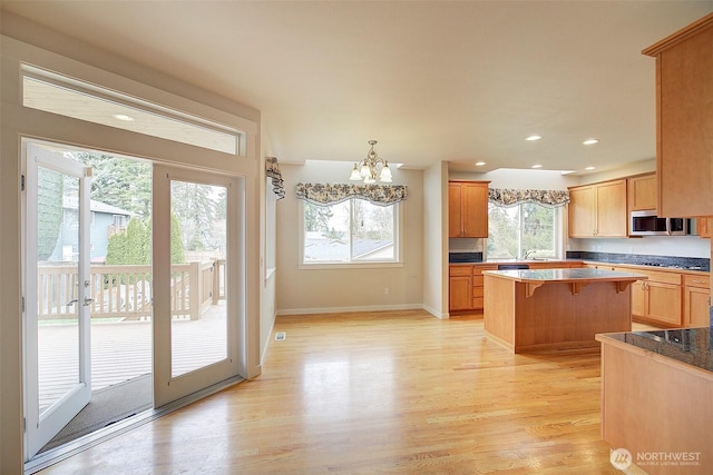 kitchen with a notable chandelier, stainless steel microwave, a kitchen breakfast bar, a center island, and light wood-style floors