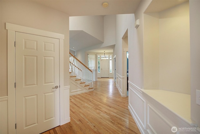 corridor featuring a wainscoted wall, light wood finished floors, stairs, a decorative wall, and a notable chandelier