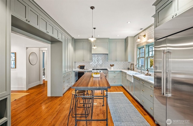 kitchen featuring butcher block countertops, high quality appliances, a breakfast bar area, gray cabinetry, and a sink