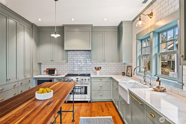 kitchen featuring gray cabinetry, butcher block counters, a sink, hanging light fixtures, and high end stainless steel range oven