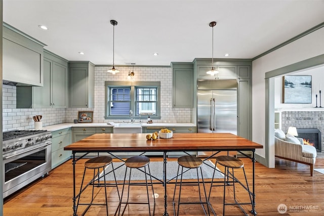 kitchen with light countertops, high end appliances, light wood-type flooring, and a tile fireplace