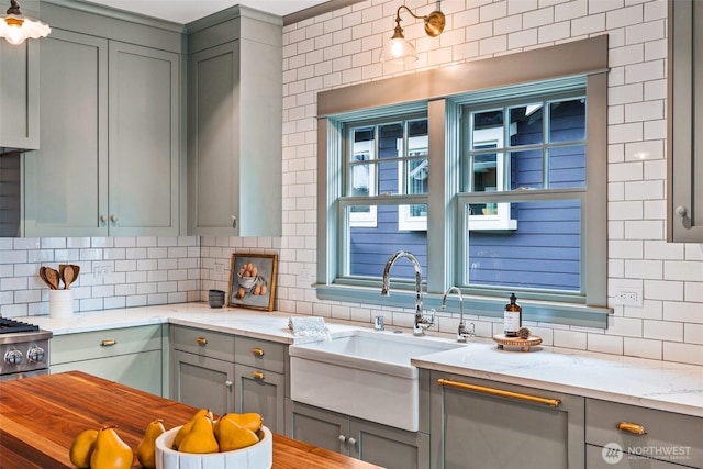 kitchen featuring gray cabinets, a sink, backsplash, and light stone countertops