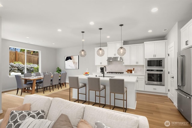 kitchen with under cabinet range hood, a breakfast bar, a sink, open floor plan, and appliances with stainless steel finishes