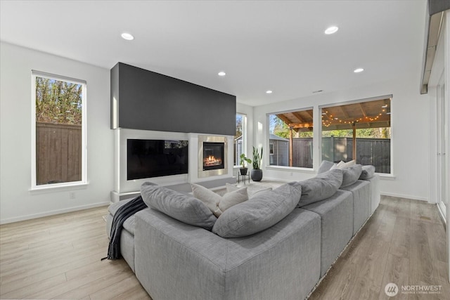 living room with a glass covered fireplace, recessed lighting, baseboards, and light wood-style floors