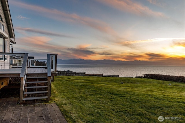 yard at dusk featuring a deck with water view and stairway